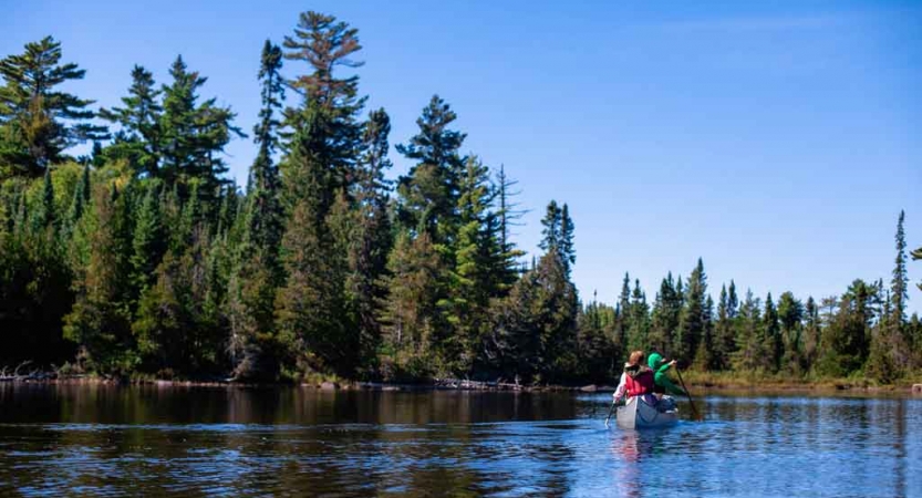 a canoe is paddled by outward bound students on calm waters beside tall green trees